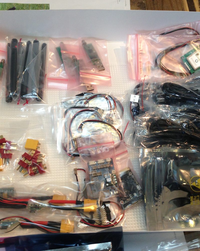 A tray of drone electronics in plastic bags: radio modules and antennas, a GPS unit, cables and battery connectors.