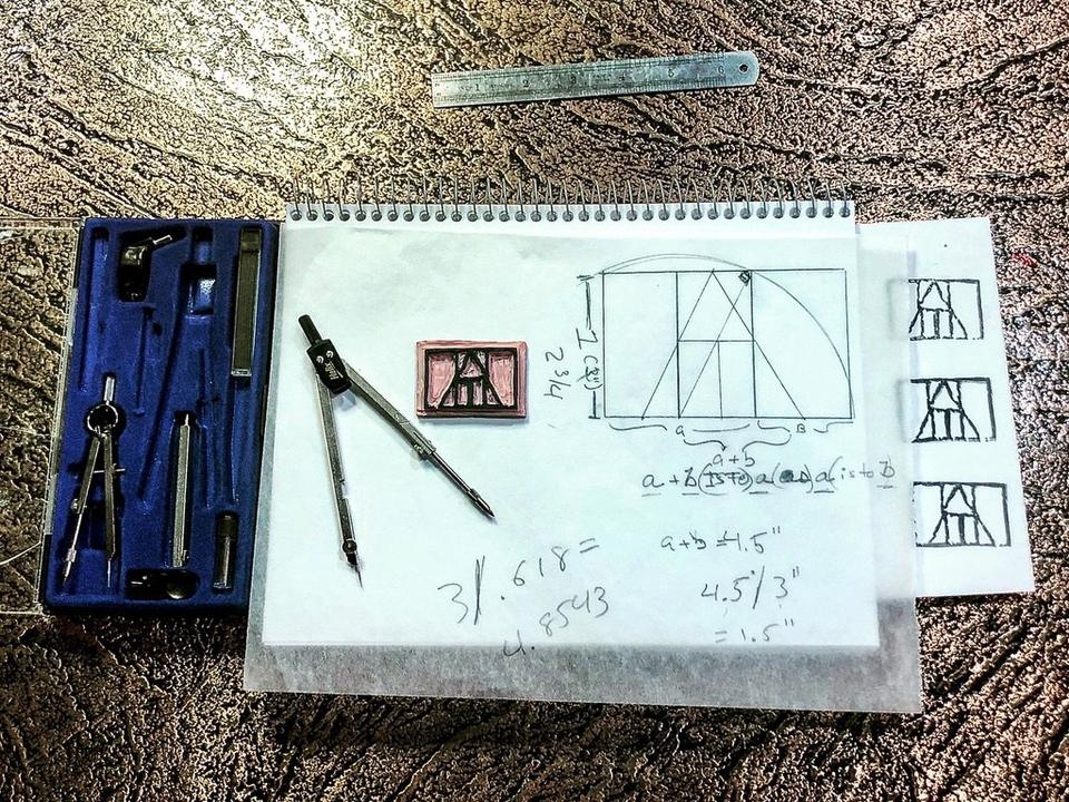 A drafting table: a compass set in a blue case, a compass, the carved stamp, a golden-section drawing of the mark and three inked versions of it.